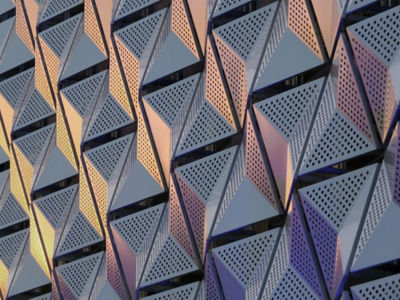 modern steel cladding with angular geometric patterns  and square holes in a shiny metallic finish with colored reflection on the wall of a car park in leeds university district
