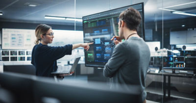 Two Diverse Software Developers Having a Meeting in a Conference Room. Female and Male Tech Industry Engineers Brainstorming Ideas for Their Neural Network Blockchain Startup